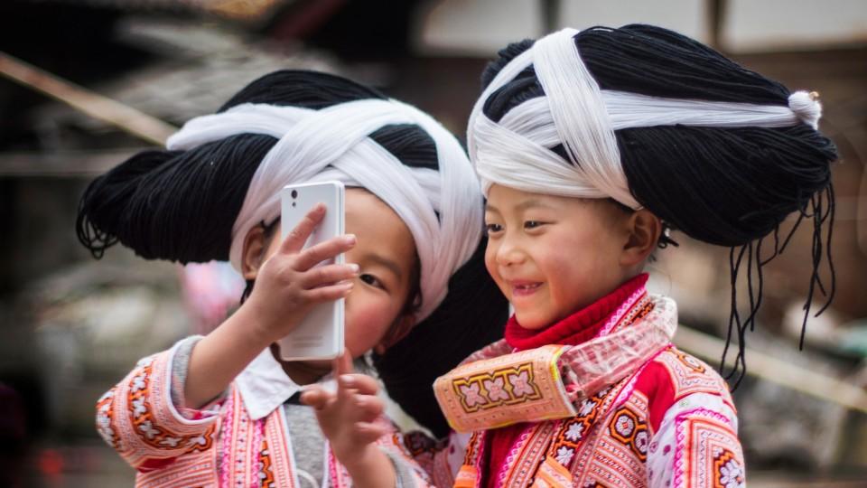 Rituale Mädchen des Long Horn Miao-Volks in China posieren für ein Selfie mit ihren großen Perücken, das von den Haaren ihrer Vorfahren gemacht wurde.