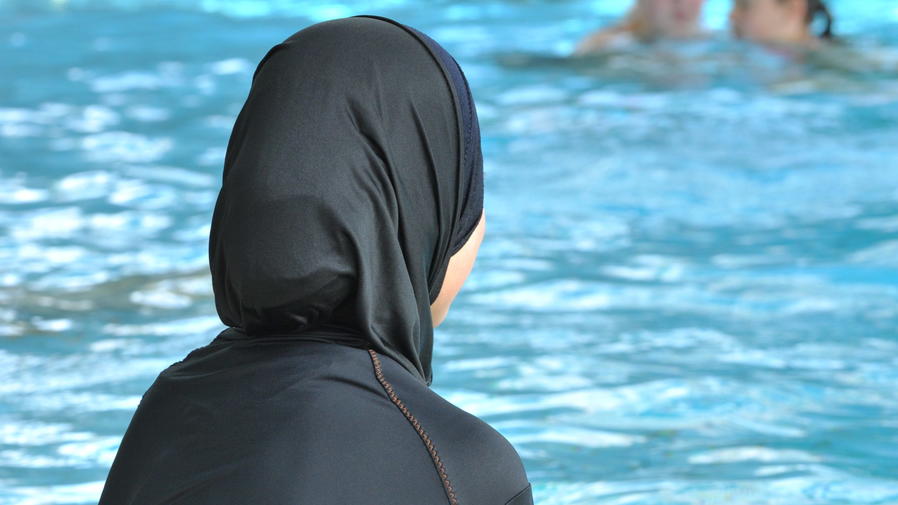 EuGH-Urteil: Muslimische Schülerin muss zum Schwimmunterricht Eine muslimische Schülerin sitzt in einem Burkini am Rande eines Schwimmbeckens.