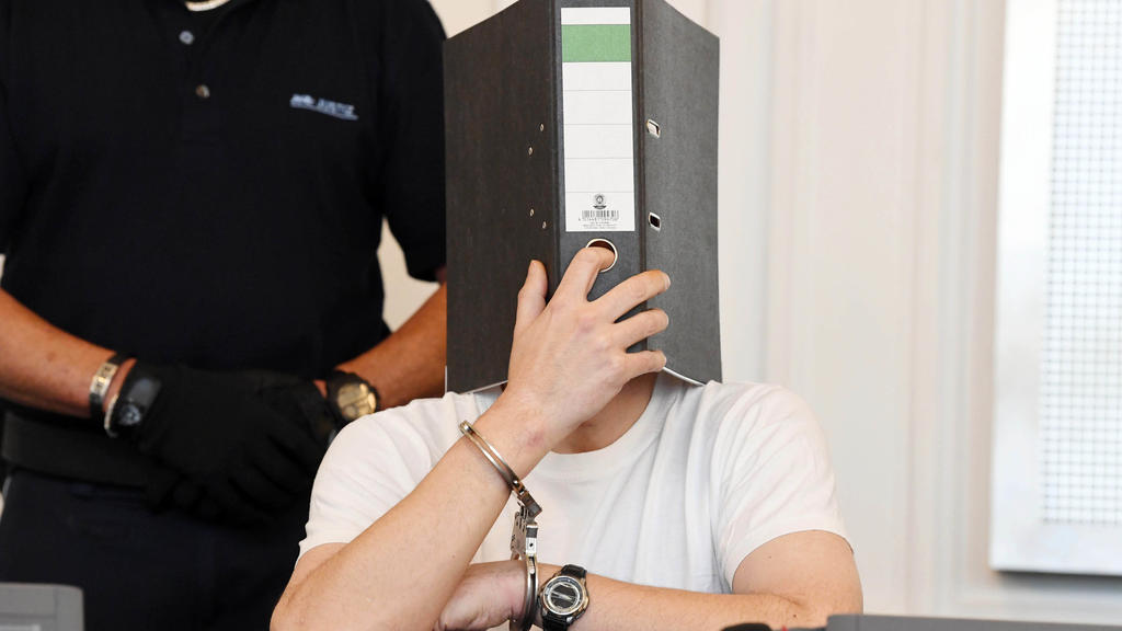 29.06.2018, Baden-Württemberg, Karlsruhe: Der 44 Jahre alte Angeklagte in einem Missbrauchsprozess verdeckt bei der Fortführung der Verhandlung in einem Sitzungssaal im Landgericht sein Gesicht mit einem Aktenordner. Das Gericht will an diesem Freita