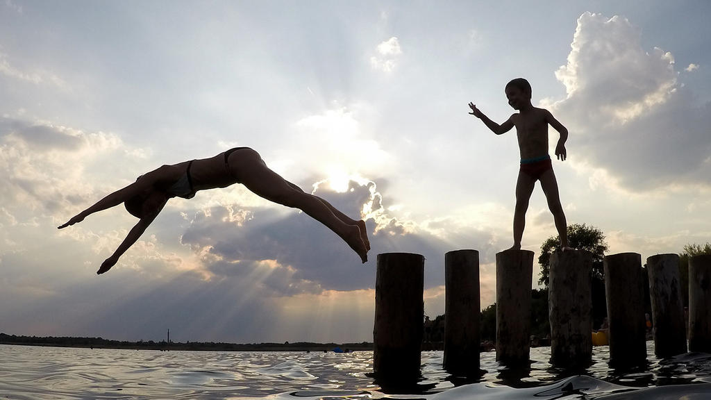 ARCHIV - 31.07.2018, Sachsen, Markkleeberg: Eine junge Frau springt von einer Buhne in den Markkleeberger See. Sonnenschein pur, Schweiß und Hitze: Von dem wochenlangen Hochsommer dieses Jahres haben nicht alle touristischen Angebote gleichermaßen pr