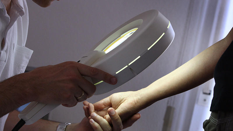 Ein Hautarzt untersucht mit einem Vergrößerungsglas die Haut einer Patientin bei einer Hautkrebs-Früherkennung. Im Kampf gegen die Ausbreitung von Krebs müssen Regierungen w