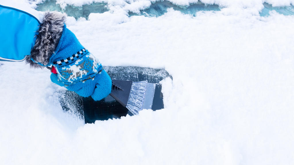 Mensch befreit Autoscheibe von Schnee und Eis.