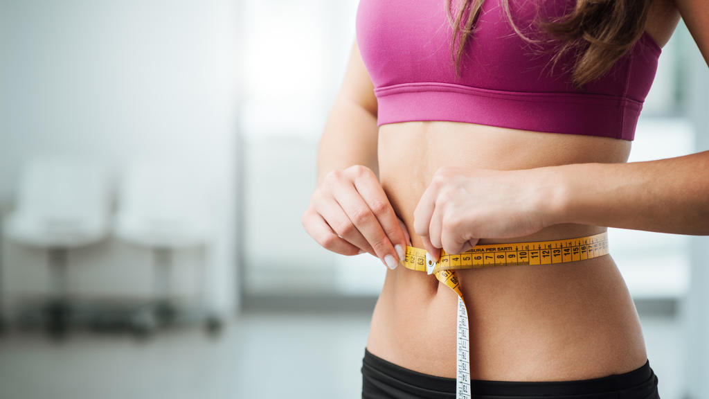 Frau misst ihre Taille mit Maßband.