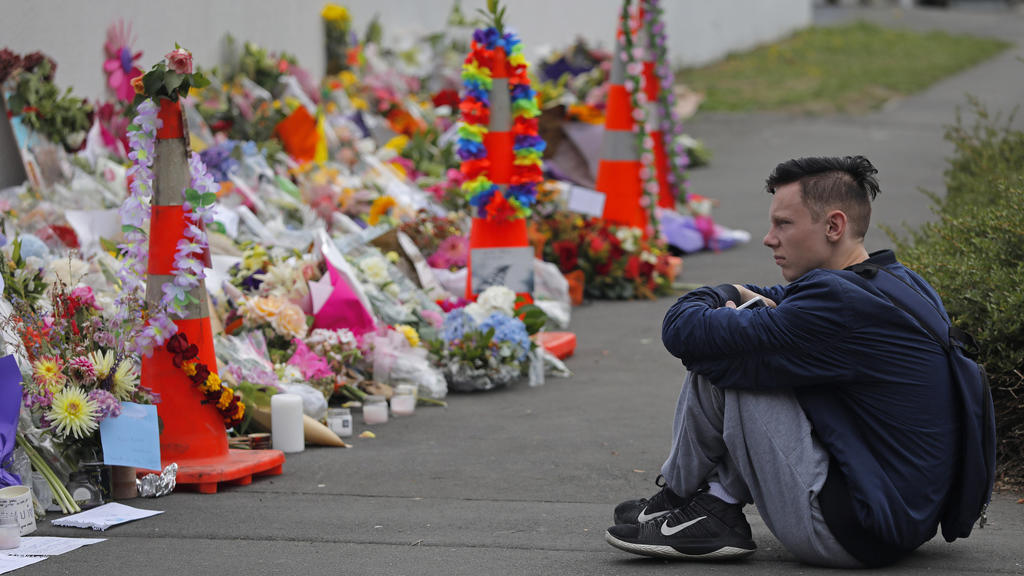 18.03.2019, Neuseeland, Christchurch: Ein Schüler sitzt vor Blumen, die in Gedenken an die Opfer des Anschlages niedergelegt wurden. Das Massaker mit mindestens 50 Todesopfern in zwei Moscheen im neuseeländischen Christchurch geht allem Anschein nach
