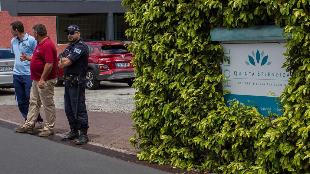 18.04.2019, Portugal, Canico: Vor dem Hotel «Quinta Splendida» steht ein Polizist neben zwei Männern. Hier waren die Businsassen des Busunglücks untergebracht, bei dem am 17.04.2019 auf der portugiesischen Atlantikinsel Madeira 29 Menschen ums Leben