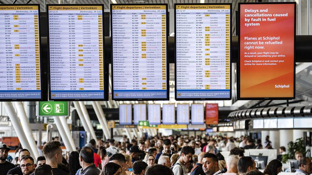 24.07.2019, Niederlande, Amsterdam: Zahlreiche Fluggäste warten am Flughafen Schiphol unter Anzeigetafeln mit einem Hinweis: "Delays and cancellations caused by fault in fuel system. Planes at Schiphol cannot be refuelled right now." (Verspätungen un