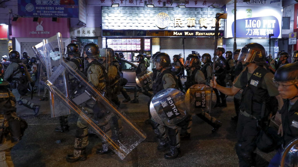 17.08.2019, China, Hongkong: Polizisten in Schutzausrüstung gehen an Läden vorbei während eines Protests prodemokratischer Demonstranten. Mit einer Kundgebung für Freiheit und Demokratie hat am Samstag in Hongkong ein neues Protest-Wochenende begonne