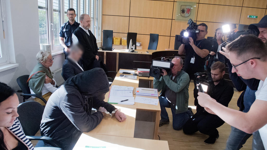 20.08.2019, Mecklenburg-Vorpommern, Stralsund: Der 19-jähriger Angeklagte (2.v.l.) verbirgt im Gerichtssaal im Landgericht sein Gesicht. Für den Mord an der 18-jährigen Maria aus Zinnowitz auf Usedom müssen sich am selben Tag der 19- und ein 21-Jähri