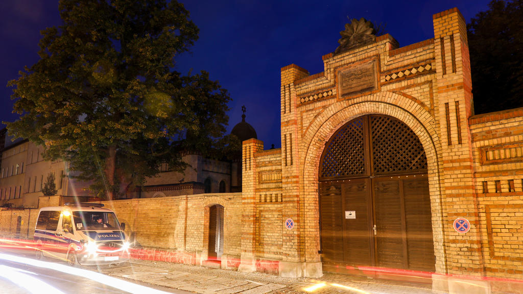 10.10.2019, Sachsen-Anhalt, Halle: Polizisten in einem Polizeifahrzeug stehen vor der Synagoge in Halle. Am Vortag hatte hier ein schwerbewaffneter Täter versucht, in die Synagoge einzudringen und dort unter Dutzenden Gläubigen ein Blutbad anzurichte