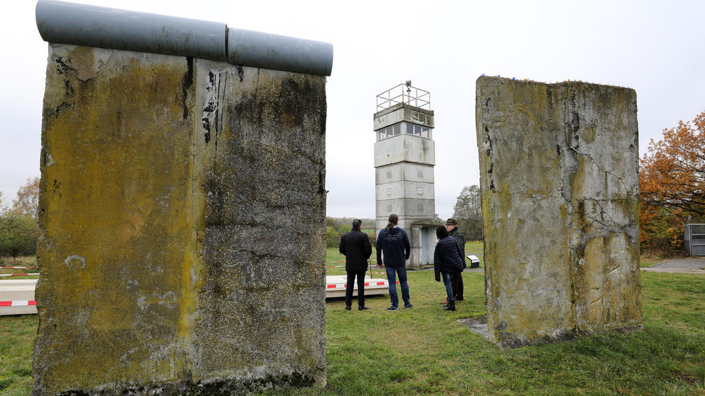 07.11.2019, Mecklenburg-Vorpommern, Schlagsdorf: Einen Grenz-Beobachtungsturm aus den 60er Jahren zwischen Elementen der Betonsperrmauer der ehemaligen innerdeutsche Grenze schauen sich Besucher auf dem Freigelände vom Grenzhus Schlagsdorf an. Mit za