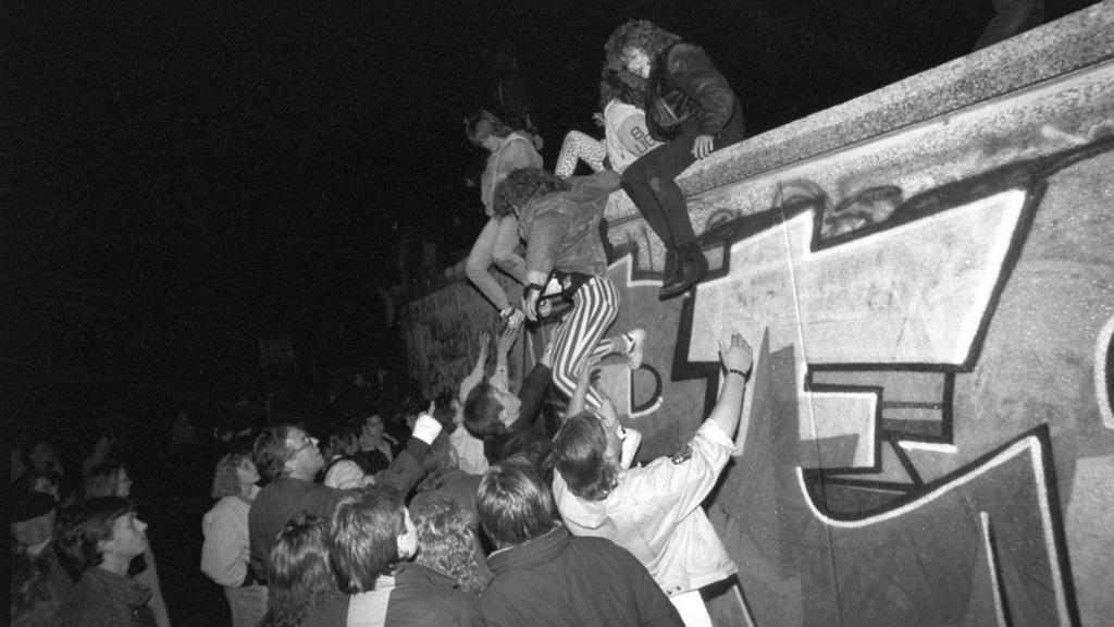 ARCHIV - 09.11.1989, Berlin: Menschen klettern am späten Abend auf die Berliner Mauer am Brandenburger Tor. Am Abend des 09.11.1989 teilte SED-Politbüro Mitglied Schabowski mit, daß alle DDR-Grenzen in die Bundesrepublik und nach West-Berlin für DDR-