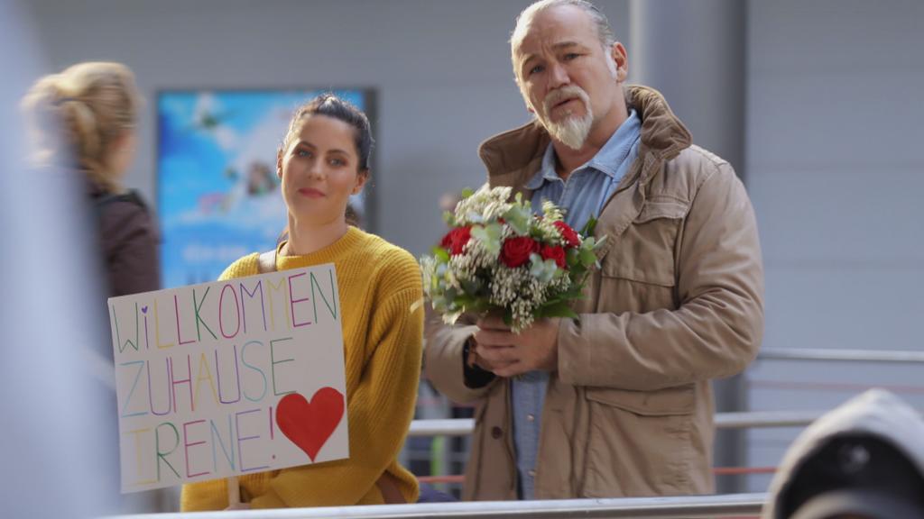Unter uns: Sina und Robert stehen am Flughafen und warten auf Irene.