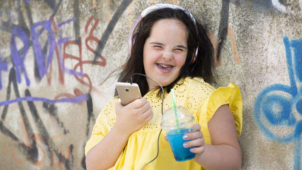 Teenager with down syndrome using smartphone, holding plastic cup model released Symbolfoto PUBLICATIONxINxGERxSUIxAUTxHUNxONLY ERRF00271