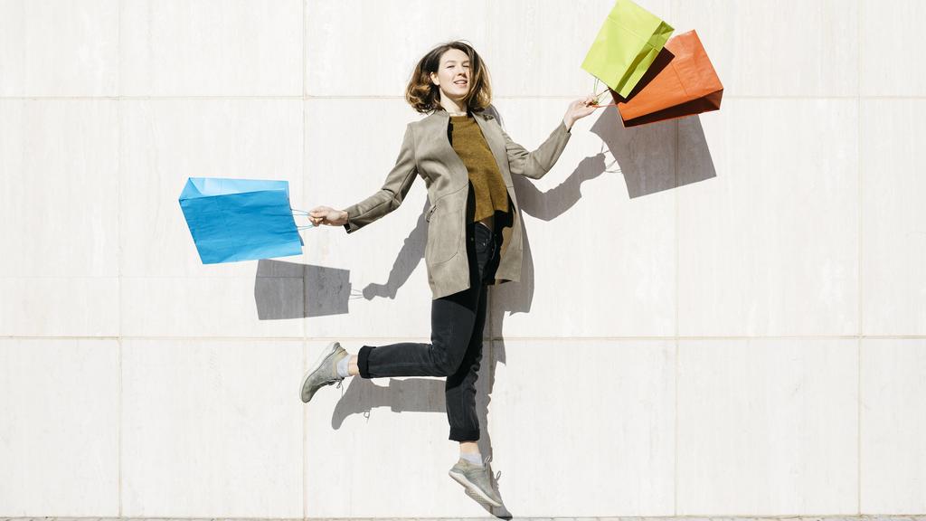 Cheerful woman with shopping bags jumping at a wall model released Symbolfoto PUBLICATIONxINxGERxSUIxAUTxHUNxONLY JRFF02783