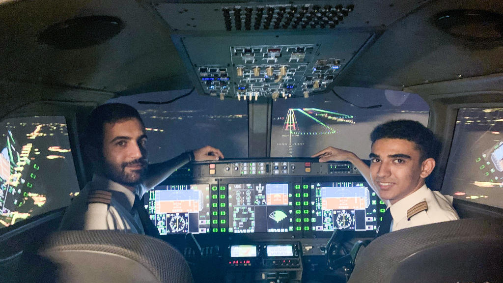 Seth Van Beek (right) who has become the UK's youngest qualified commercial pilot aged just 18. He is pictured here with colleague Paris Antoino in a flight simulator at the Egnatia Aviation Training college. See SWNS sto