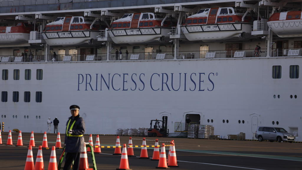 A security guard stands near the quarantined Diamond Princess cruise ship Thursday, Feb. 13, 2020, in Yokohama, near Tokyo. Life on board the luxury cruise ship, which has dozens of cases of a new virus, can include fear, excitement and soul-crushing