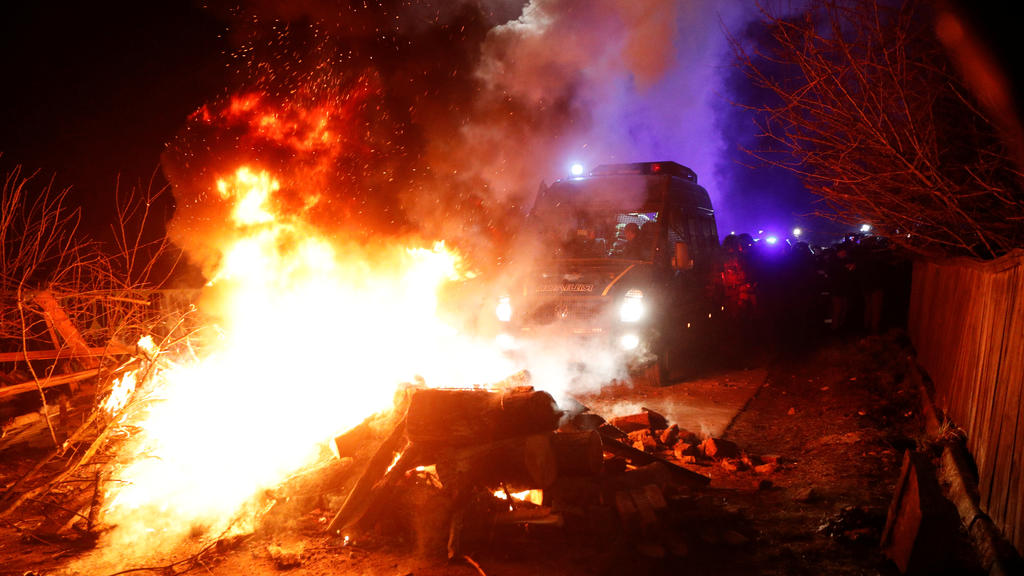 Ukrainian law enforcement officers and firefighters clear the way as demonstrators block a road during a protest against the arrival of a plane carrying evacuees from coronavirus-hit China's Hubei province in the village of Novi Sanzhary in Poltava r