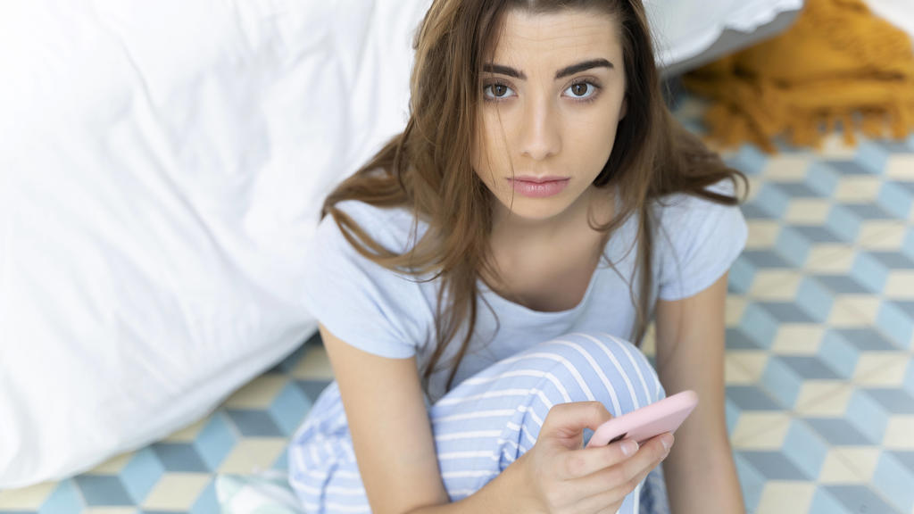 Junge Frau hält sorgenvoll ihr Smartphone in der Hand.