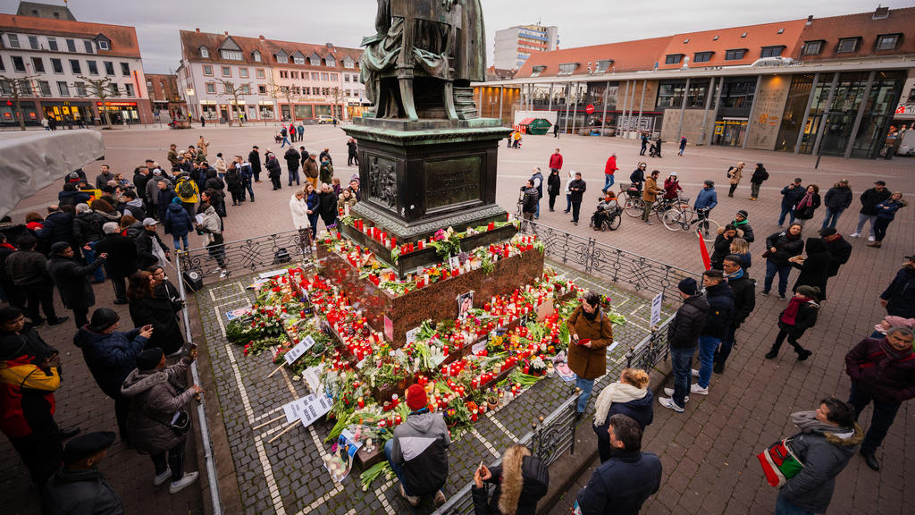 22.02.2020, Hessen, Hanau: Menschen stehen um das Brüder-Grimm-Nationaldenkmal an dem zum Gedenken an die Anschläge Blumen niedergelegt wurden. Bei einem mutmaßlich rassistischen Anschlag hatte ein 43-jähriger Deutscher im hessischen Hanau mehrere Me
