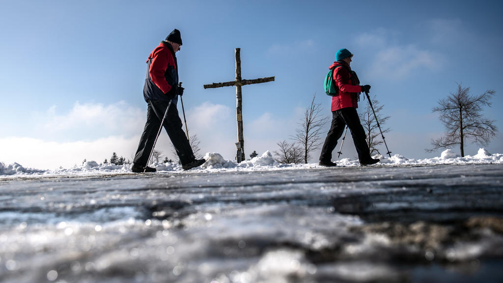 07.02.2020, Nordrhein-Westfalen, Winterberg: Wanderer gehen auf dem verschneiten Kahlen Asten unter blauem Himmel an einem Kreuz vorbei. Foto: Bernd Thissen/dpa +++ dpa-Bildfunk +++