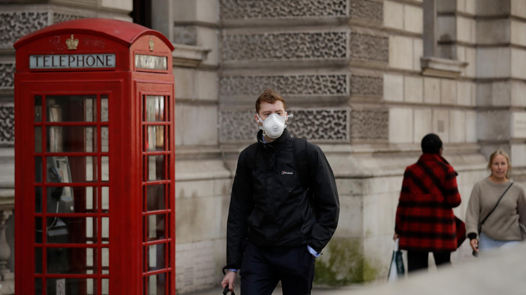 11.03.2020, Großbritannien, London: Ein Mann mit Mundschutz geht an einer roten Telefonzelle in der Nähe des Parliament Square vorbei. Foto: Matt Dunham/AP/dpa +++ dpa-Bildfunk +++