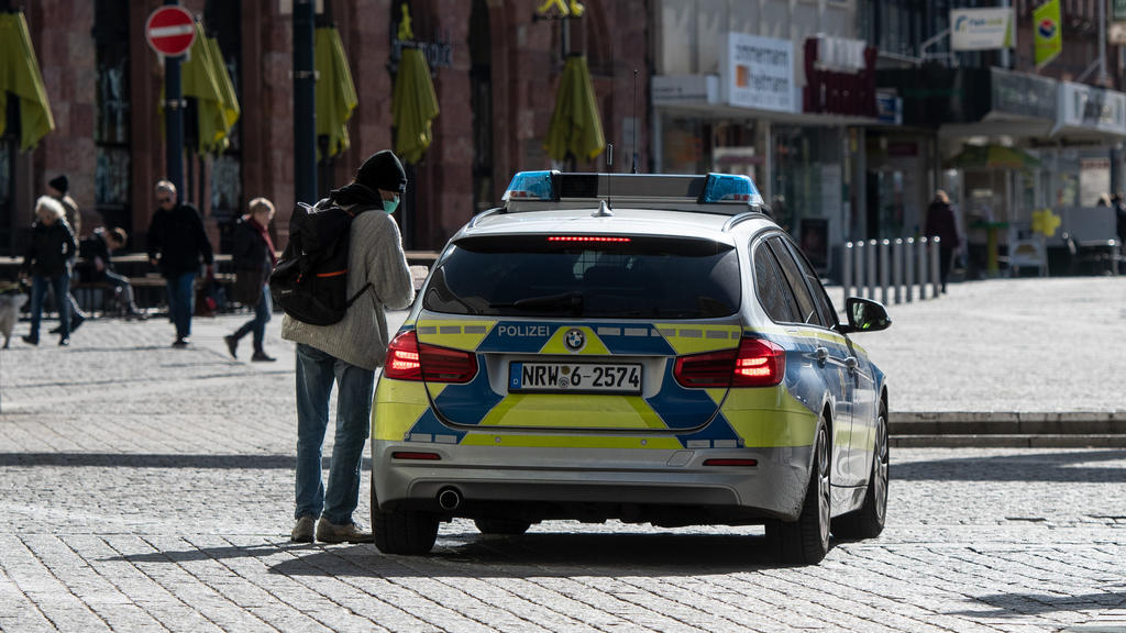 ARCHIV - 23.03.2020, Nordrhein-Westfalen, Dortmund: Ein Mann mit einem Mundschutz unterhält sich in der Fußgängerzone mit den Polizisten in einem Streifenwagen. Nordrhein-Westfalen hat einen Bußgeldkatalog für Verstöße gegen die landesweiten Corona-R