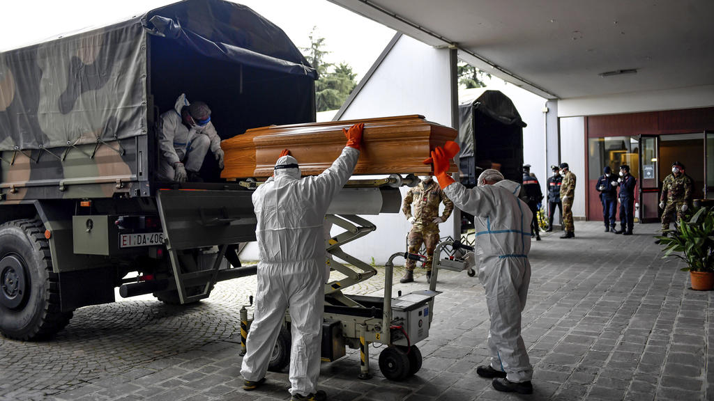 27.03.2020, Italien, Cinisello Balsamo: Särge, die aus der Gegend von Bergamo eintreffen, werden von Arbeitern in Schutzanzügen aus einem Militärfahrzeug in ein Gebäude des Friedhofs von Cinisello Balsamo getragen. Foto: Claudio Furlan/LaPresse/AP/dp