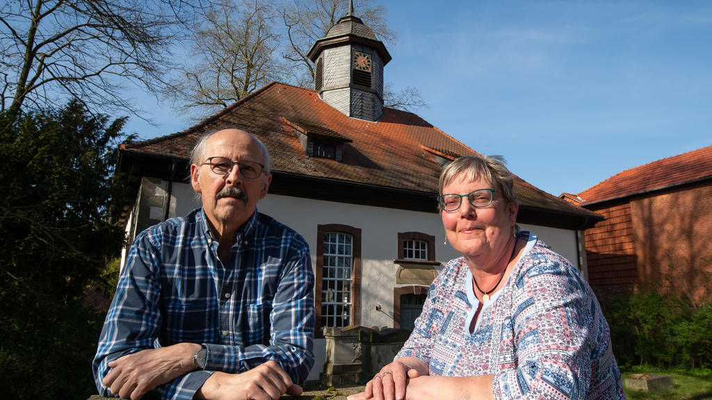 16.04.2020, Niedersachsen, Löwenhagen: Das Ehepaar Uwe Kamm (SPD), stellvertretender Bürgermeister, und Roswitha Kamm, Kirchenvorsteherin, stehen vor der Kirche Löwenhagen mit ihrem kleinen Kirchturm.