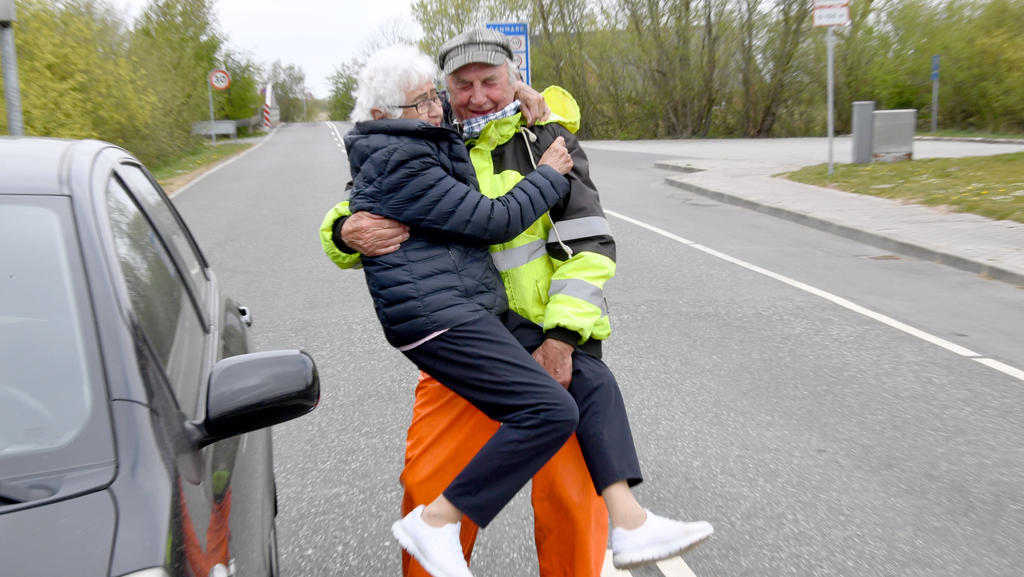 24.04.2020, Schleswig-Holstein, Aventoft: Inga Rasmussen aus Dänemark (85) wird von Karsten Tüchsen Hansen (89) aus Nordfriesland bei ihrem täglchen Treffen an der deutsch-dänischen Grenze hochgehoben. Nach Schließung der Grenze am 14.03.2020 hatten