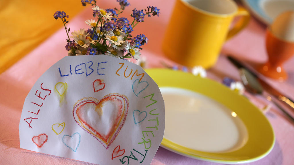 ARCHIV - 07.05.2017, Bayern, Kaufbeuren: An einem Strauß Blumen auf einem gedeckten Frühstückstisch lehnt ein Papier mit der Aufschrift «Alles Liebe zum Muttertag». (Zu dpa 