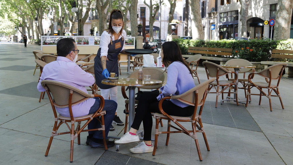 05.05.2020, Spain, Palma: on the day of the reopening, a waitress serves coffee to two guests on the terrace of a bar in Palma. As of Monday, in phase 1 of the relaxation of the crown measures, bars, restaurants, shops.