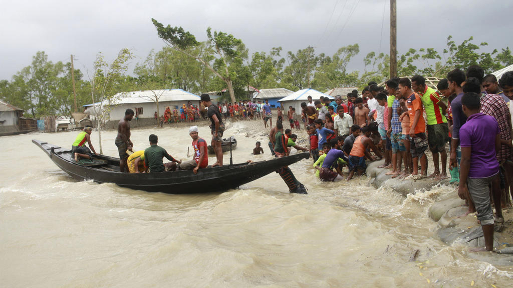 20.05.2020, Bangladesch, Shyamnagar: Ein Boot bringt vor der Ankunft des Zyklons «Amphan» Menschen ans Land, während Einheimische einen Damm überprüfen. Der Wirbelsturm hat in Indien und Bangladesch über zehn Menschen das Leben gekostet. Sie starben