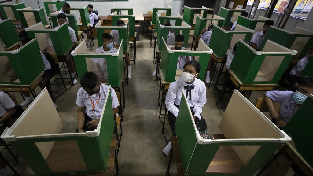 01.07.2020, Thailand, Pathum Thani: Schülerinnen und Schüler, die zur Vermeidung einer Ansteckung mit dem Coronavirus Mundschutze tragen, sitzen mit Abstand zueinander an Pulten mit U-förmigen Wänden in einem Klassenzimmer der Schule «Samkhok School