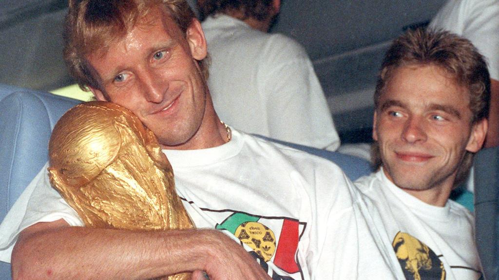 ARCHIV - 09.07.1990, Frankfurt/Main: Andreas Brehme (l), damaliger deutscher Fußballnationalspieler nimm den WM-Pokal in den Arm und sein Teamgefährte Thomas Häßler schaut lächelnd zu. (zu dpa: «Von Illgner bis Völler: Zwölf Helden in der magischen N