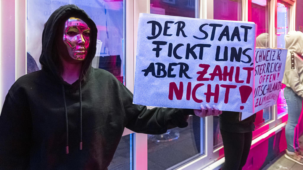 11.07.2020, Hamburg: Eine Prostituierte hält in der Herbertstraße ein Schild mit der Aufschrift «Der Staat fickt uns, aber er zahlt nicht». Sie demonstriert mit anderen Frauen für die Öffnung der Bordelle auf St. Pauli. Diese sind zur Eindämmung der