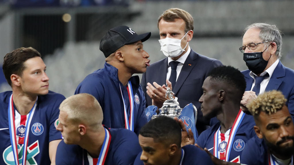 French President Emmanuel Macron, center, applauds as PSG's Kylian Mbappe, center left, walks past the trophy for the winners of the French Cup soccer final match between Paris Saint Germain and Saint Etienne at Stade de France stadium, in Saint Deni