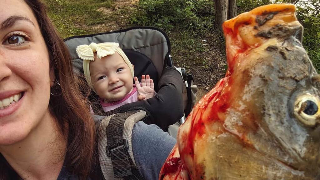 Beka Garris trägt ihre Tochter Isabella in einer Trage auf dem Rücken und einen toten Fisch in der Hand.