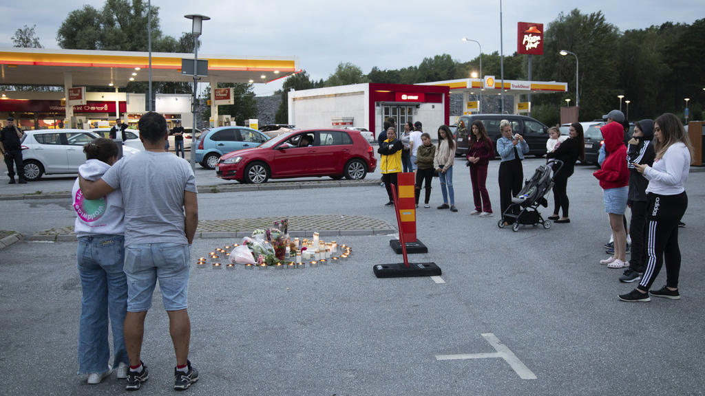 02.08.2020, Schweden, Stockholm: Menschen stehen neben Blumen und Kerzen auf einem Parkplatz nahe einer Tankstelle in Botkyrka. Ein Mädchen im Teenageralter ist in der Nacht zum Sonntag (2. August) in der Nähe einer Tankstelle in der Gemeinde Botkyrk