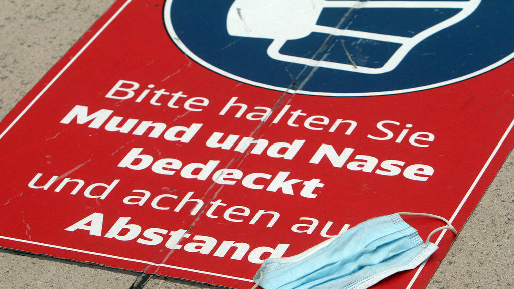 Getragene Mund-Nase-Bedeckungsmaske liegt auf einem Aufkleber mit Piktogramm Maskenpflicht und Aufschrift bitte halten Sie Mund und Nase bedeckt und achten auf den Abstand im Fernbahnhof im Flughafen Frankfurt, Hessen, Deutschland *** Worn mouth nos