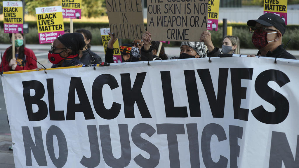 Protesters in front of the US flag flying outside the US Embassy in London, as part of an anti-racism demonstration Friday Sept. 11, 2020, coinciding with the start of the trial of the four police officers charged with the murder of George Floyd in t
