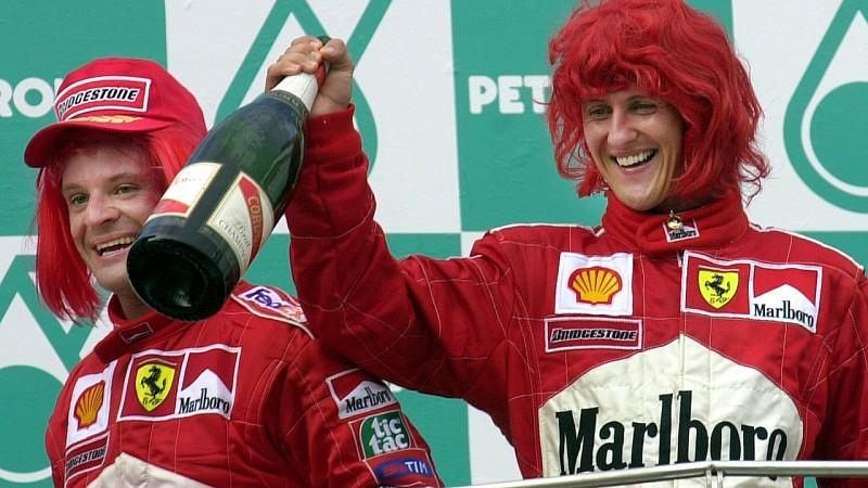 ARCHIV - Mit roten Perücken auf dem Kopf jubeln die beiden Ferrari-Piloten Michael Schumacher (Deutschland/m) und Rubens Barrichello (Brasilien/l) in Sepang nach der Siegerehrung beim Großen Preis von Malaysia (Archivfoto vom 22.10.2000). Erfolge, Sk