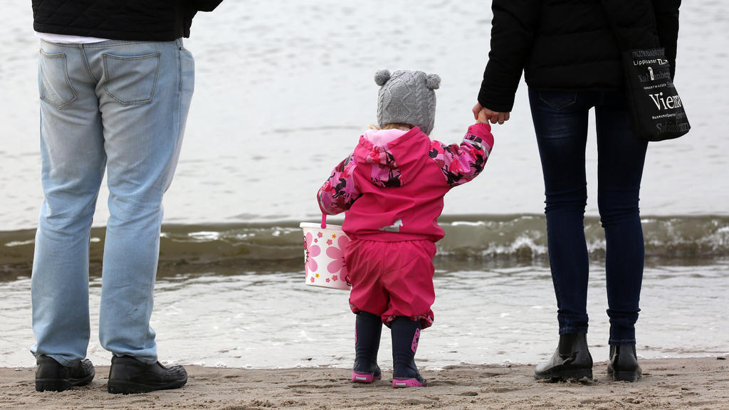ARCHIV - Eine Familie mit Kleinkind ist am 04.03.2017 am Strand des Ostseebades Warnemünde (Mecklenburg-Vorpommern) unterwegs. Die Babys von heute leben vielleicht noch länger als bisher erwartet. 2017 geborene Jungen könnten durchschnittlich bis zu