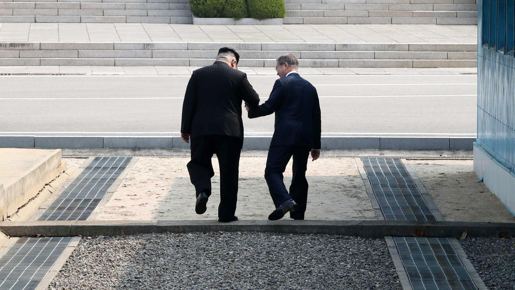 dpatopbilder - 27.04.2018, Südkorea, Panmunjom: Kim Jong Un (l), Machthaber von Nordkorea, und Moon Jae In, Präsident von Südkorea, gehen Hand in Hand über die Betonschwelle, die die Grenze zwischen ihren Ländern markiert nach Nordkorea. Als erster n