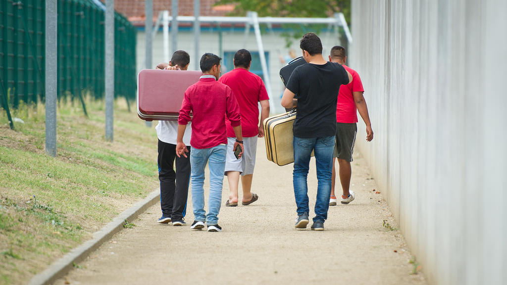 ARCHIV - 27.08.2015, Rheinland-Pfalz, Ingelheim: Flüchtlinge laufen mit Koffern bepackt auf einem Weg einer Erstaufnahmeeinrichtung für Flüchtlinge. (zu dpa «Ein Band über die Geschichte und Gegenwart der Migration» vom 14.05.2018) Foto: Christoph